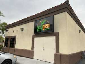 A tan and brown building with a large "EcoGen Pest Control" sign above double doors. A car is parked in front, and the sky is overcast. The building's address number is visible on the left corner, highlighting Ecogenpest services.