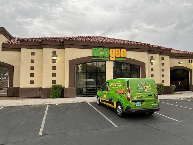 A small green van with "Ecogenpest" branding is parked in front of a tan and brown building with a sign reading "Ecogen" above the entrance. The sky is cloudy, and the mostly empty parking lot adds to the quiet scene.